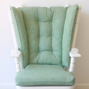 solid sage green wingback glider rocker cushions on  chair against a white wall
